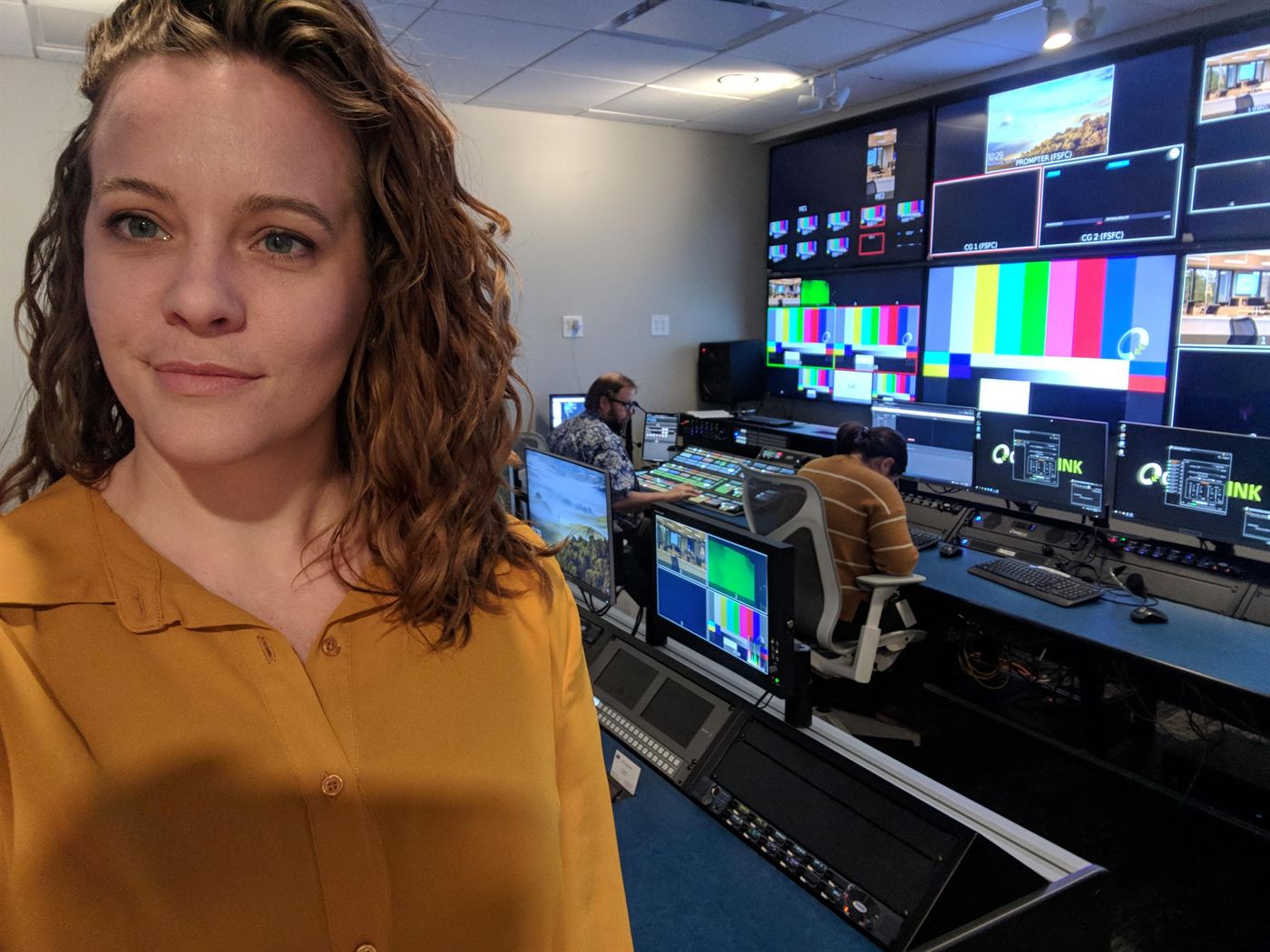 Mindy Herb in a broadcast control room, crew at the switcher and colour bars on the multiviewer wall behind her.
