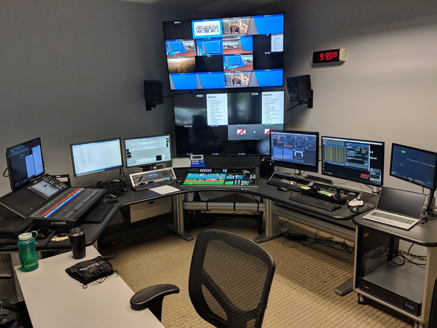 A control room desk with a Ross switcher, Yamaha audio console and a multiviewer wall showing preview and program feeds.