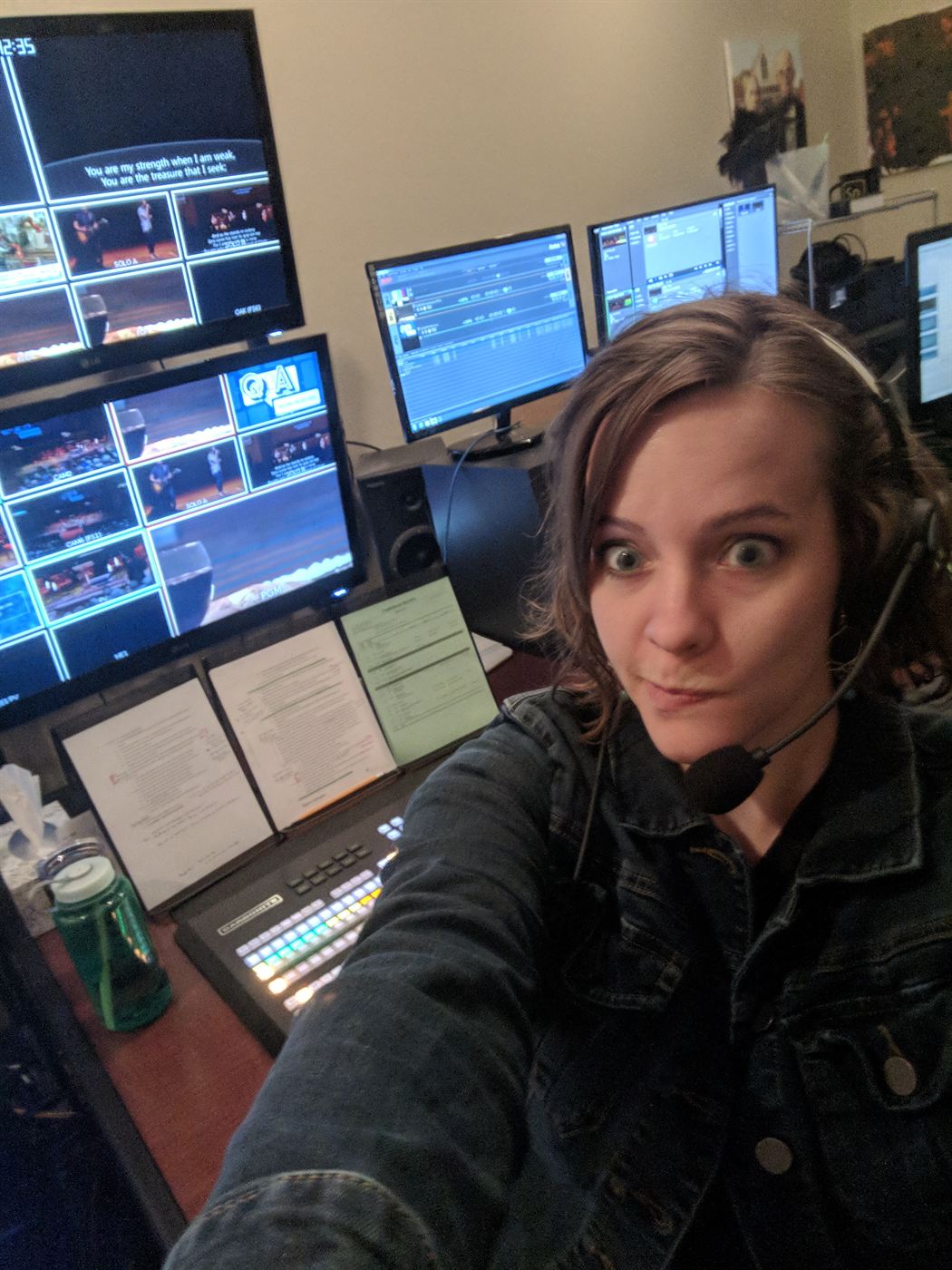 Mindy Herb on a comms headset at a switcher, directing a live service, with multiviewer screens beside her.